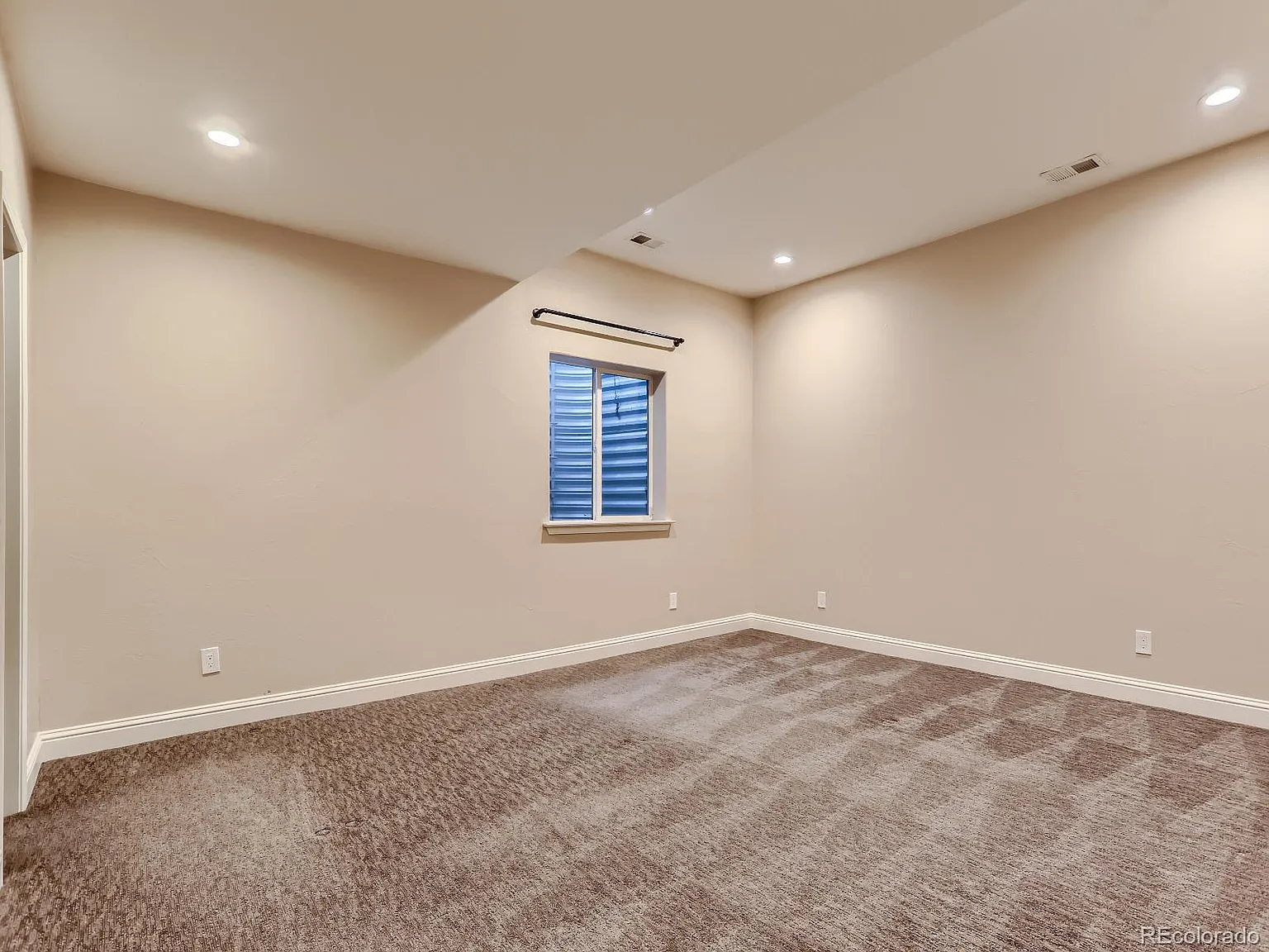 Finished basement room with neutral carpet, beige walls, and recessed lighting, offering a clean and versatile space for various uses.