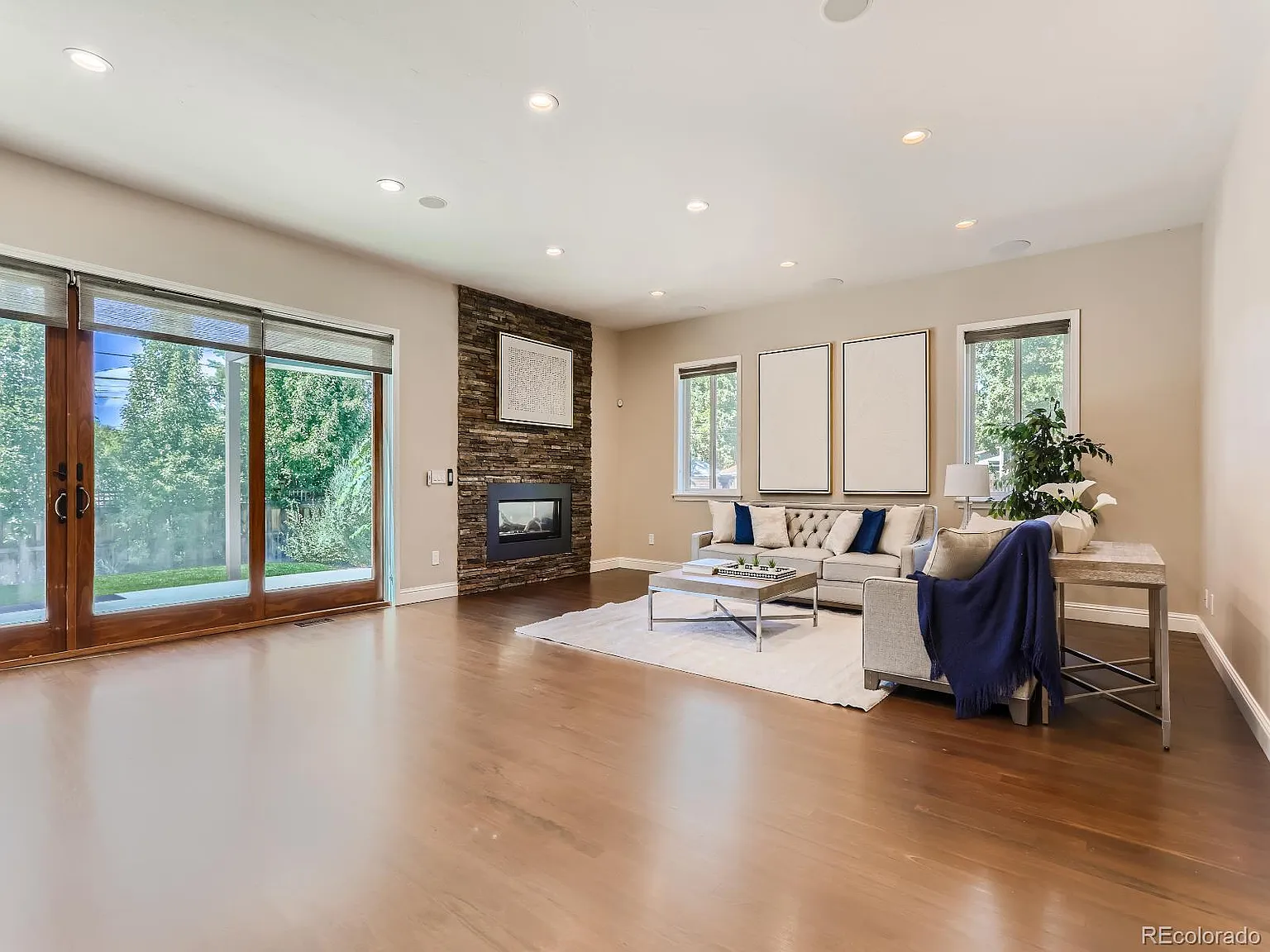 Bright and spacious living room with hardwood floors, modern fireplace, and large glass doors opening to a lush outdoor area, crafted by Denver Dream Builders.