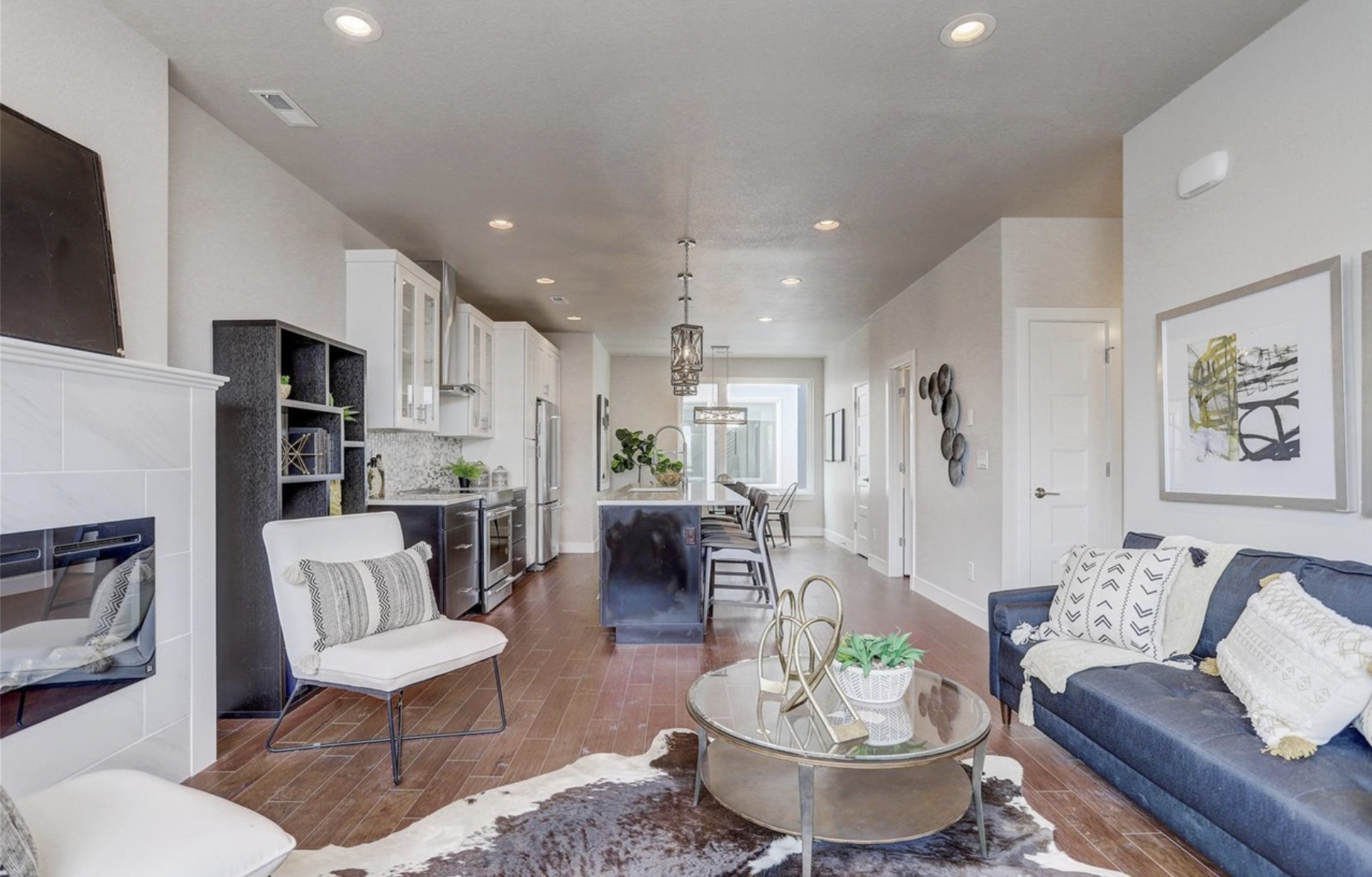 Modern open-concept living area with a cozy seating arrangement, hardwood floors, and a view into a sleek kitchen with pendant lighting.