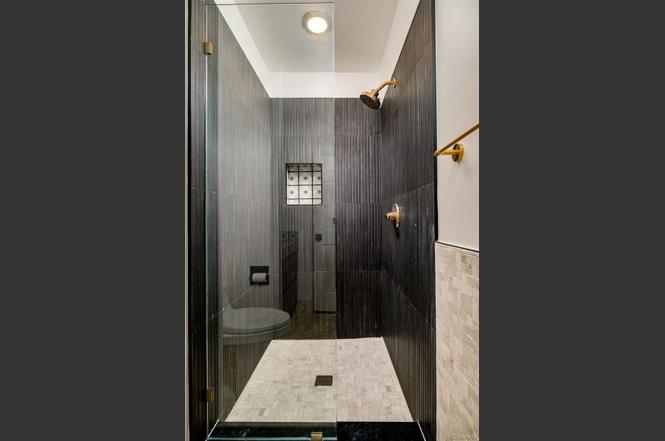 Modern walk-in shower with black tile and brass fixtures, part of a full bathroom renovation by Denver Dream Builders.