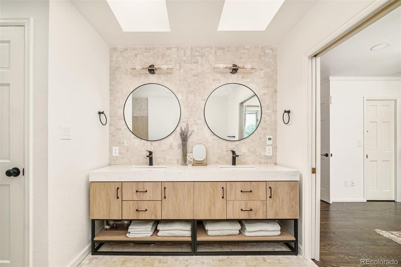 Custom double-vanity bathroom design with light wood cabinetry, dual mirrors, and warm lighting.
