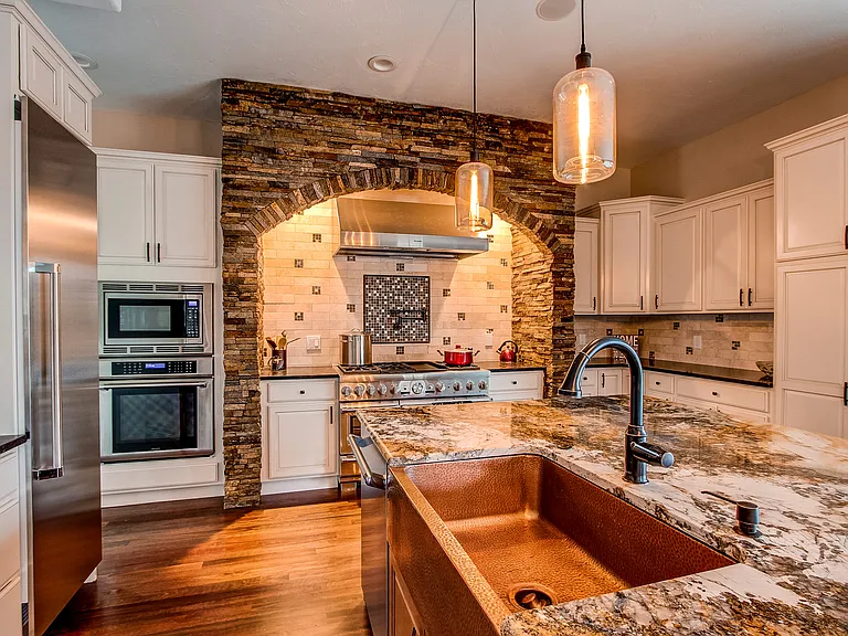 Chef’s kitchen with stone backsplash, copper farmhouse sink, and custom cabinetry with built-in appliances