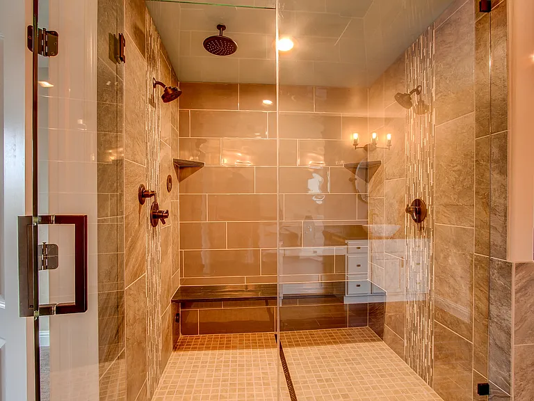 Spacious walk-in shower with dual rain showerheads, bench seating, and floor-to-ceiling tile