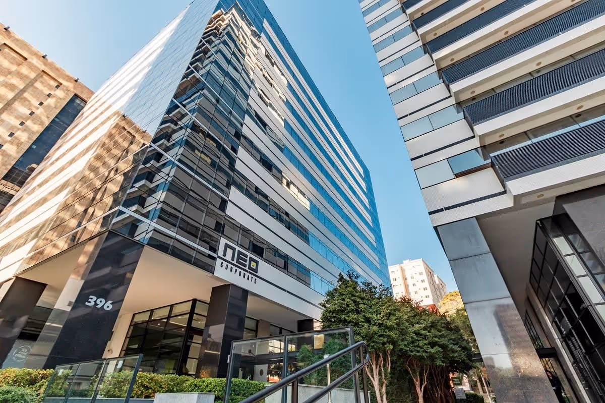 Low-angle view of a modern corporate building with glass windows and the sign 'NEO Corporate' under a clear blue sky.