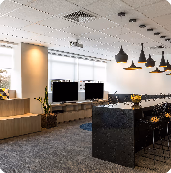 Sala de reunião moderna com mesa preta grande, cadeiras de metal, luminárias pendentes pretas e duas TVs em um móvel de madeira junto a janelas com persianas brancas.