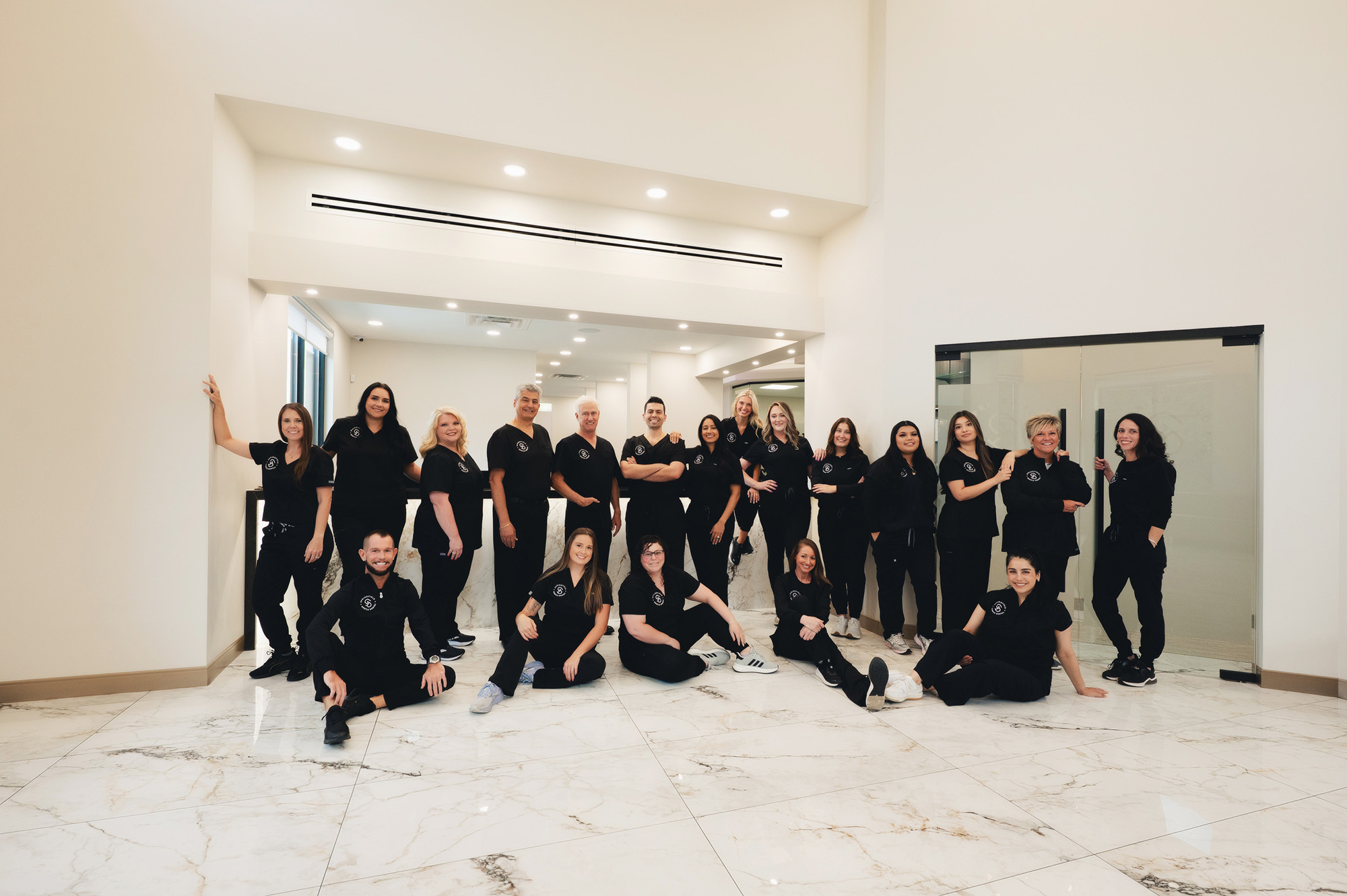 Group of medical or dental professionals in black scrubs posing in a bright, modern office lobby with marble floors.