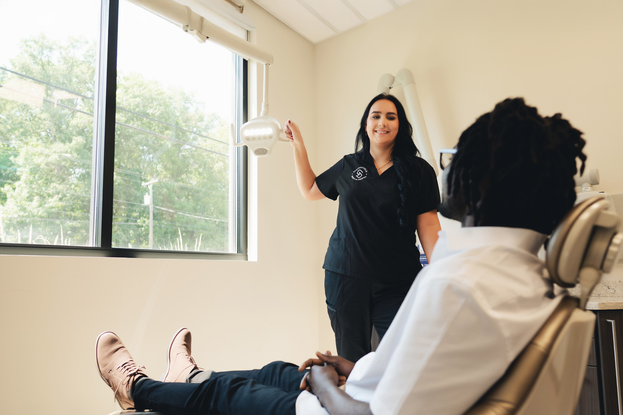 Smiling female dentist adjusting overhead light while male patient reclines in dental chair.