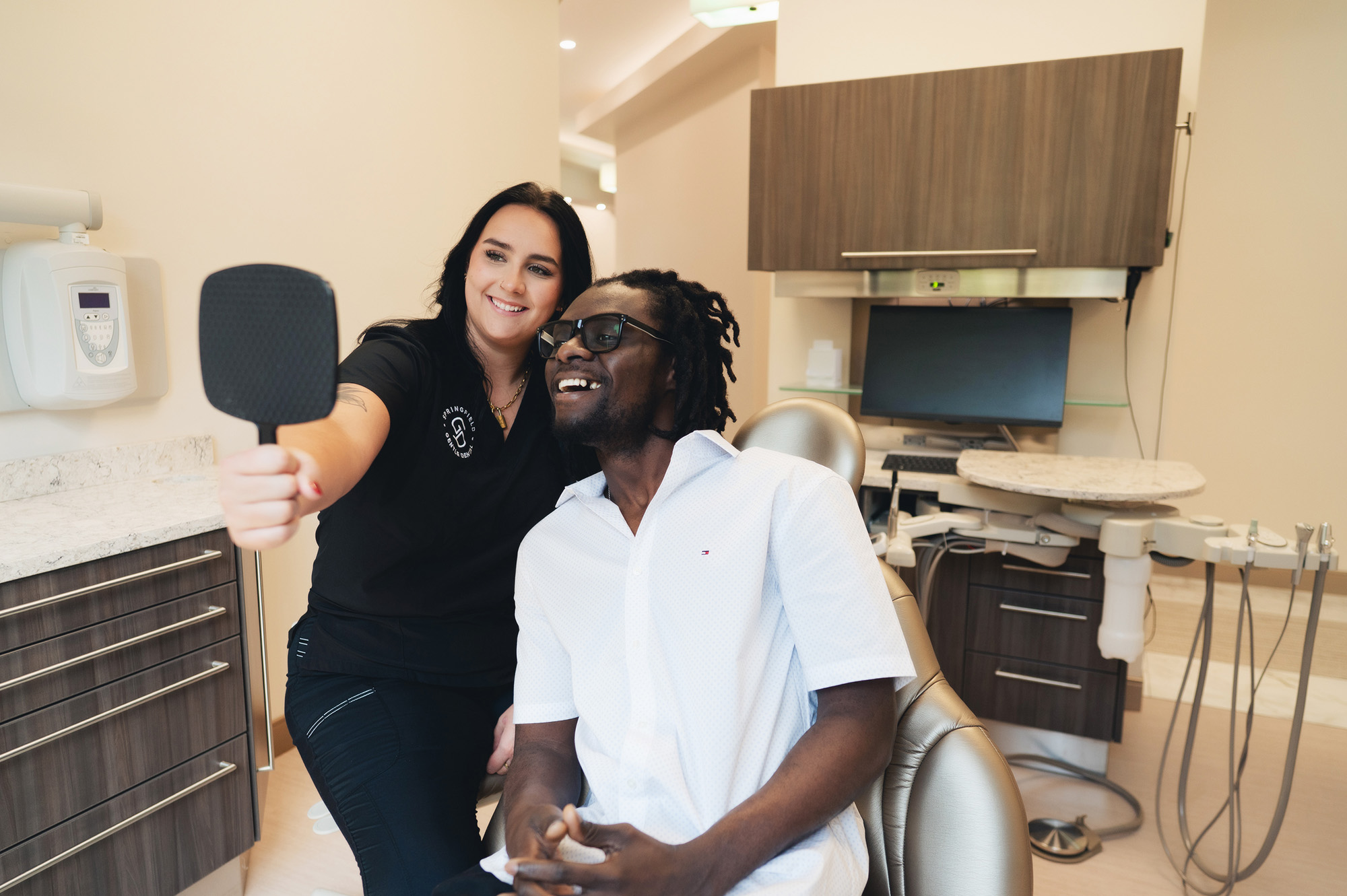 Smiling female dentist showing a mirror to a happy male patient seated in a dental chair.