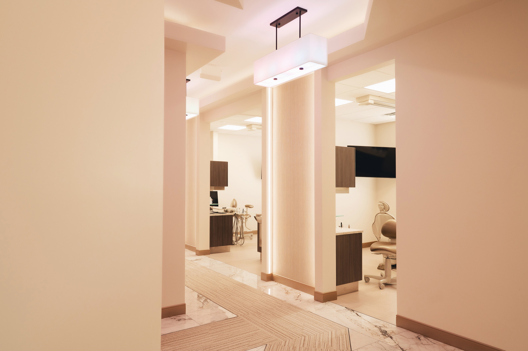 Bright, modern dental clinic hallway with treatment rooms featuring dental chairs and equipment.