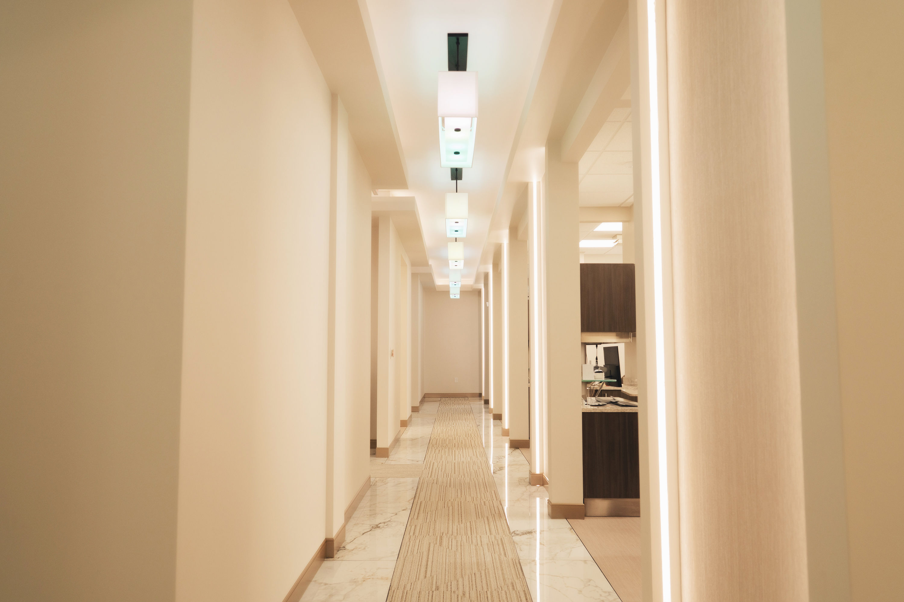 Bright, modern hallway with cream-colored walls, tiled floor, and recessed lighting leading to office spaces.