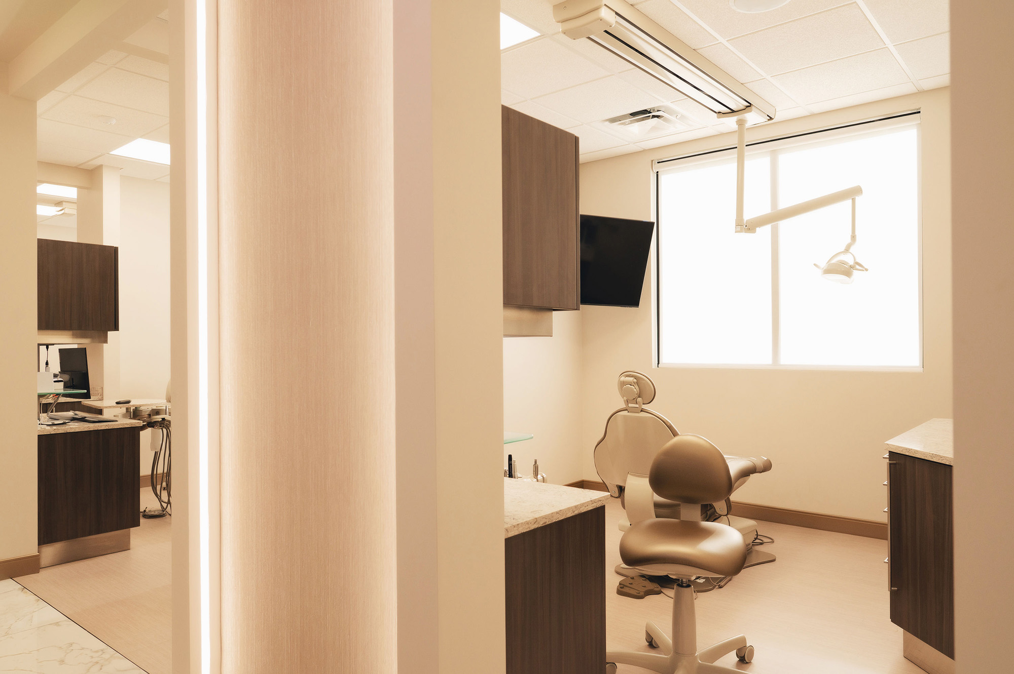 Modern dental office with a dental chair, overhead light, cabinets, and a large window providing natural light.
