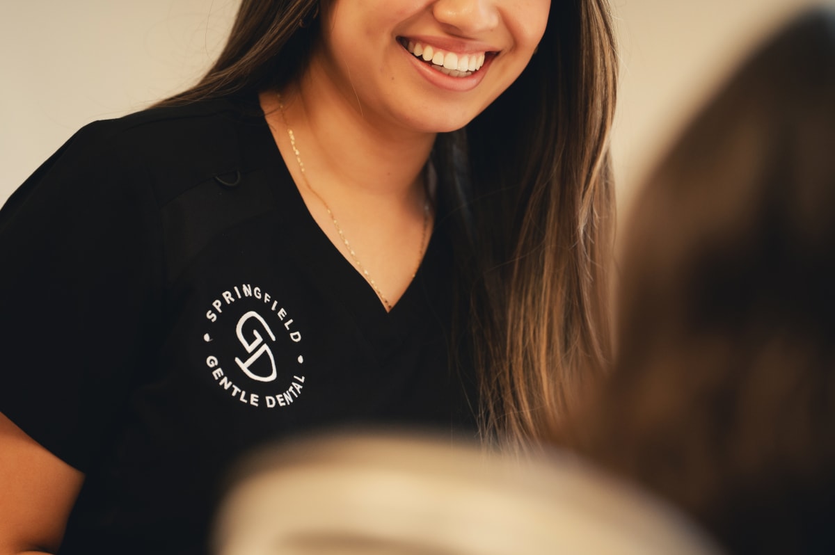 Female dental professional smiling at camera wearing black uniform with practice logo