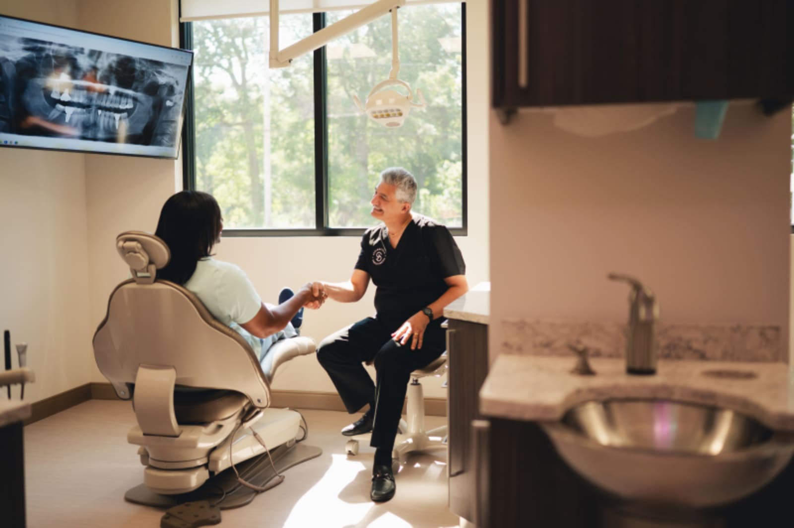 Dentist consulting with patient in treatment room with digital display