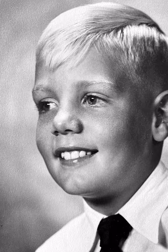 Black and white portrait of a smiling young boy with short blonde hair wearing a white shirt and dark tie.