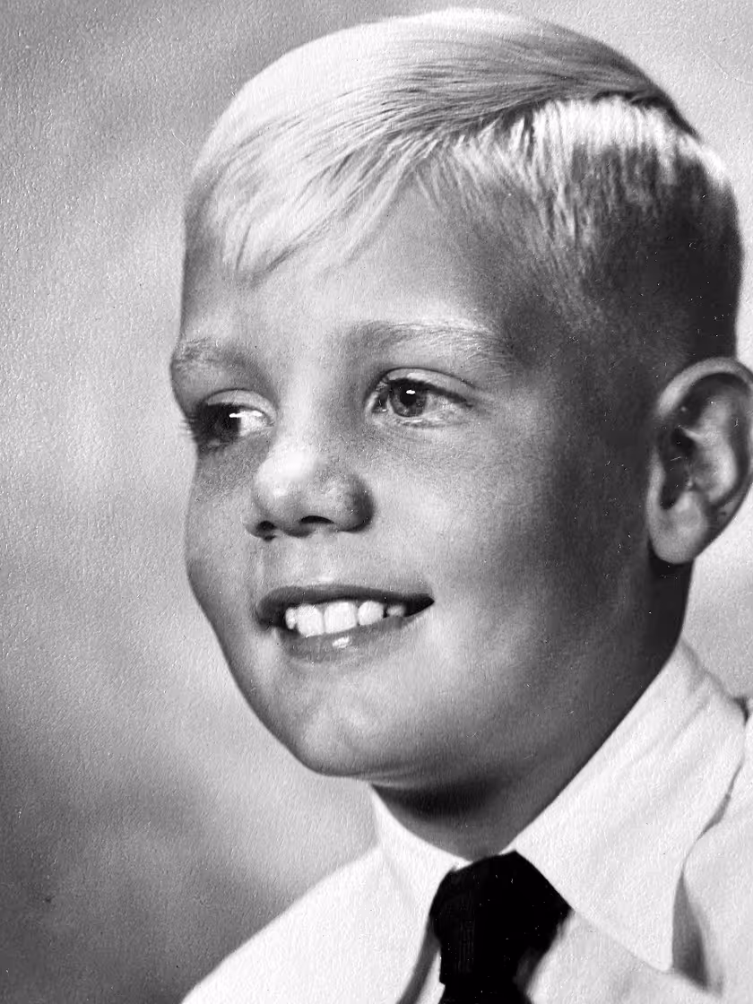 Black and white portrait of a smiling young Philip Wood with light hair, wearing a white shirt and dark tie.