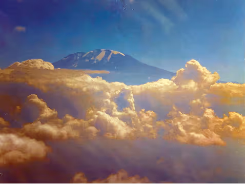 Snow-capped mountain peak rising above thick, golden clouds under a blue sky.
