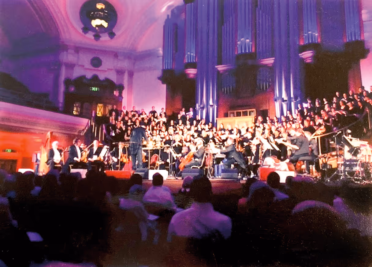 Orchestra and choir performing inside a large cathedral with purple lighting and organ pipes in the background.