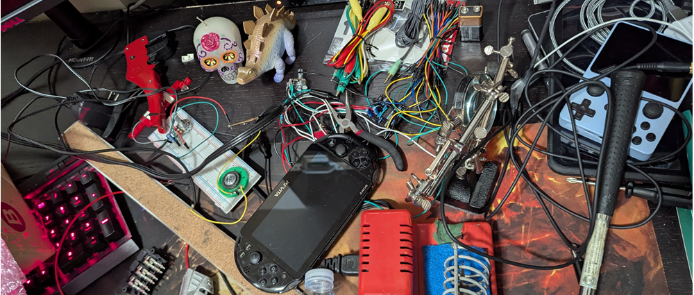 electronics strewn across a desk, modded psvita, and soldering iron visible too
