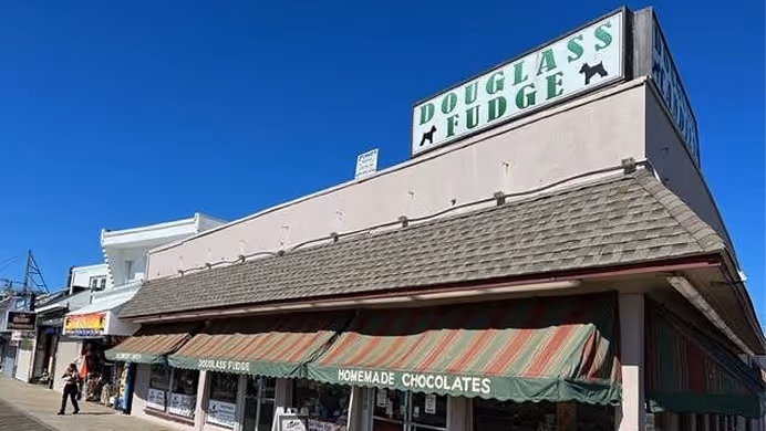 Exterior view of Douglass Fudge store with striped awnings advertising homemade chocolates under clear blue sky.