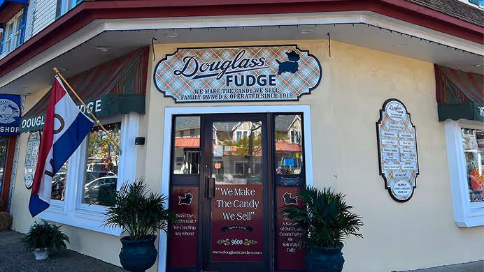 Exterior of Douglass Fudge store with signage stating it is family owned since 1919 and a flag displayed outside.
