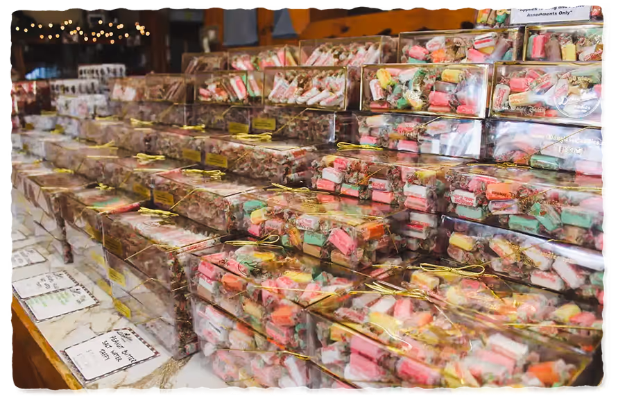 Rows of clear plastic boxes filled with colorful saltwater taffy candy stacked on a wooden counter in a store.
