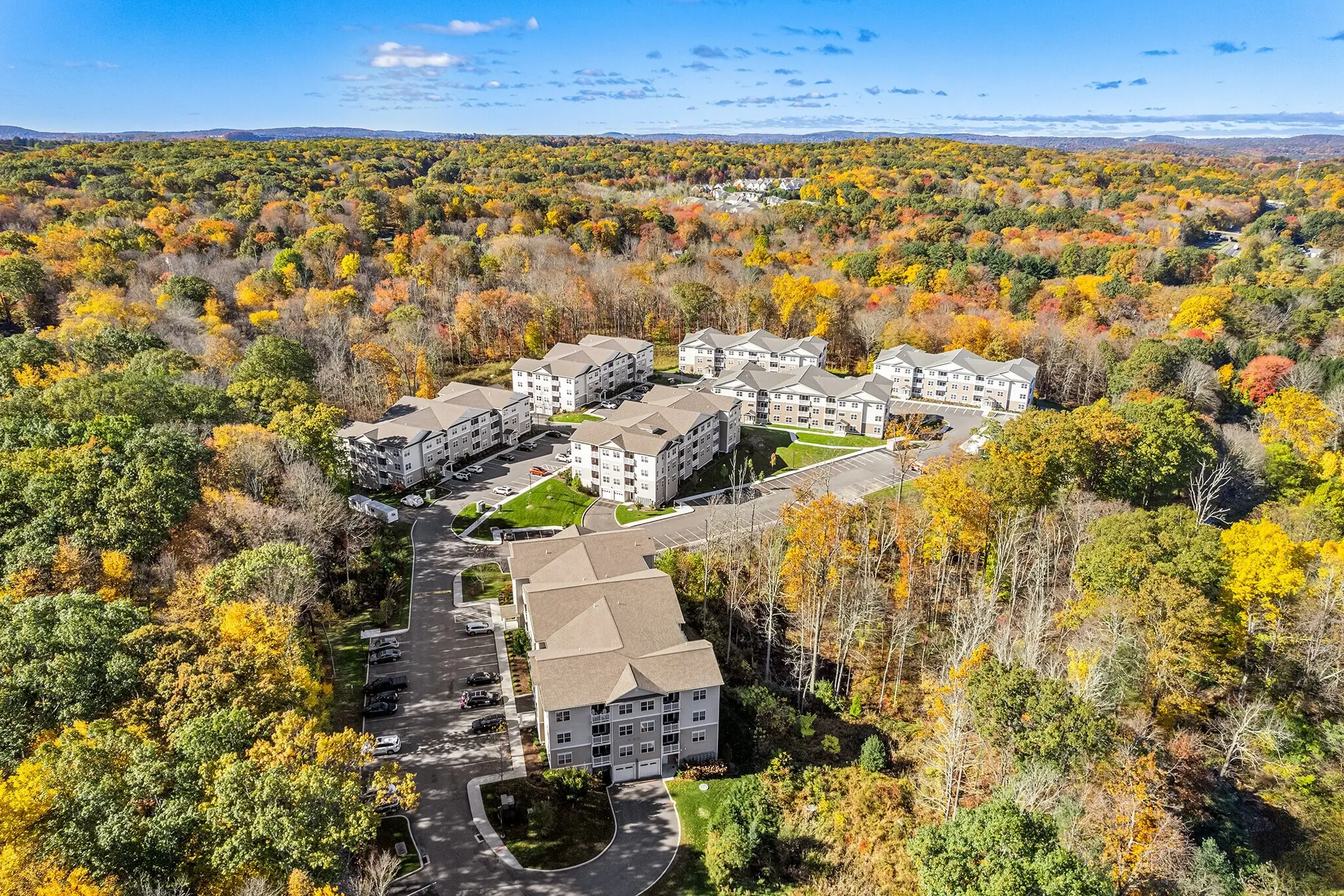Exterior view of the luxury Covered Bridge apartments in Newtown, CT, with green surroundings and spacious parking"
