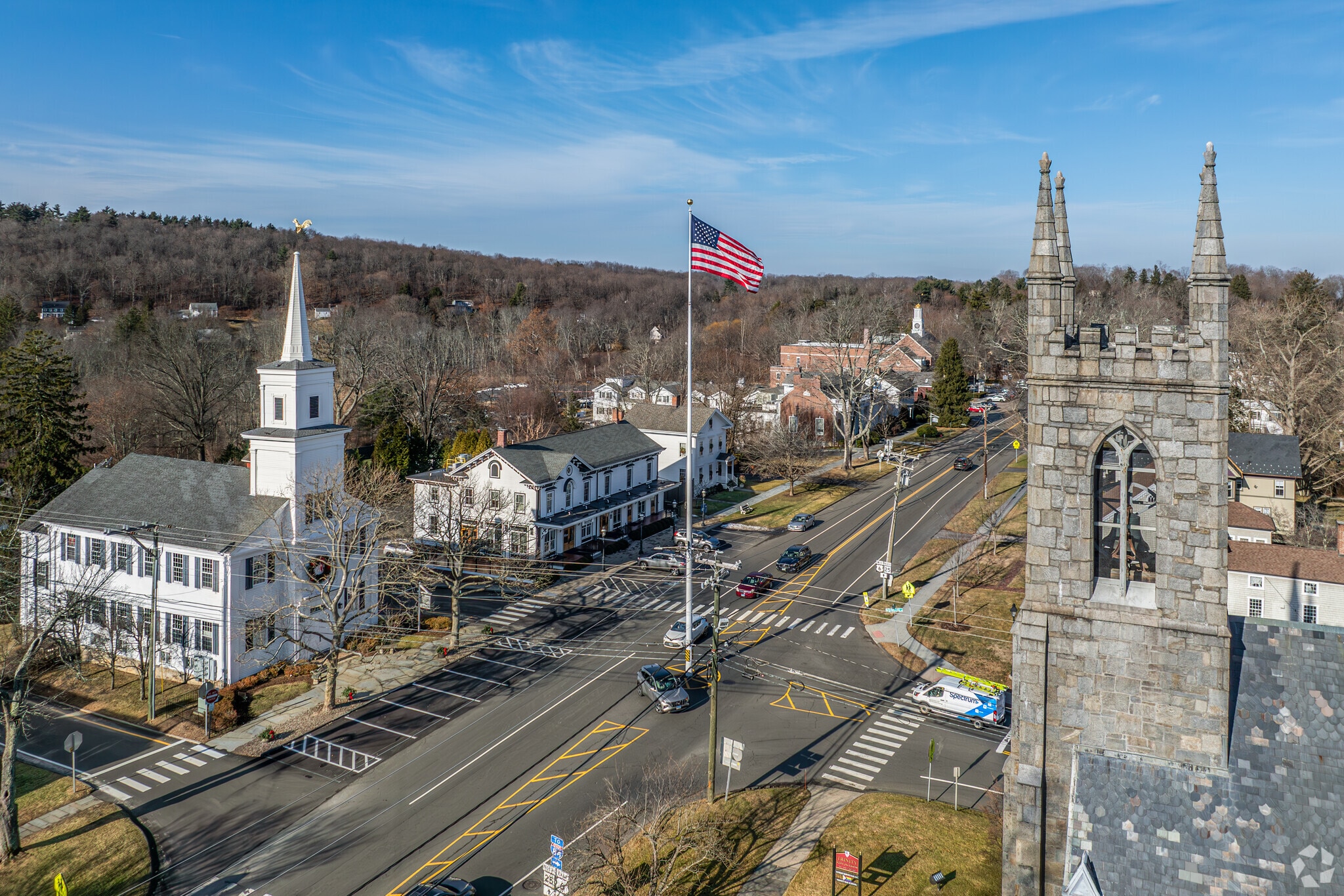 Aerial view of Newtown CT, intersection with churches, cars, and an American flag on a clear day.