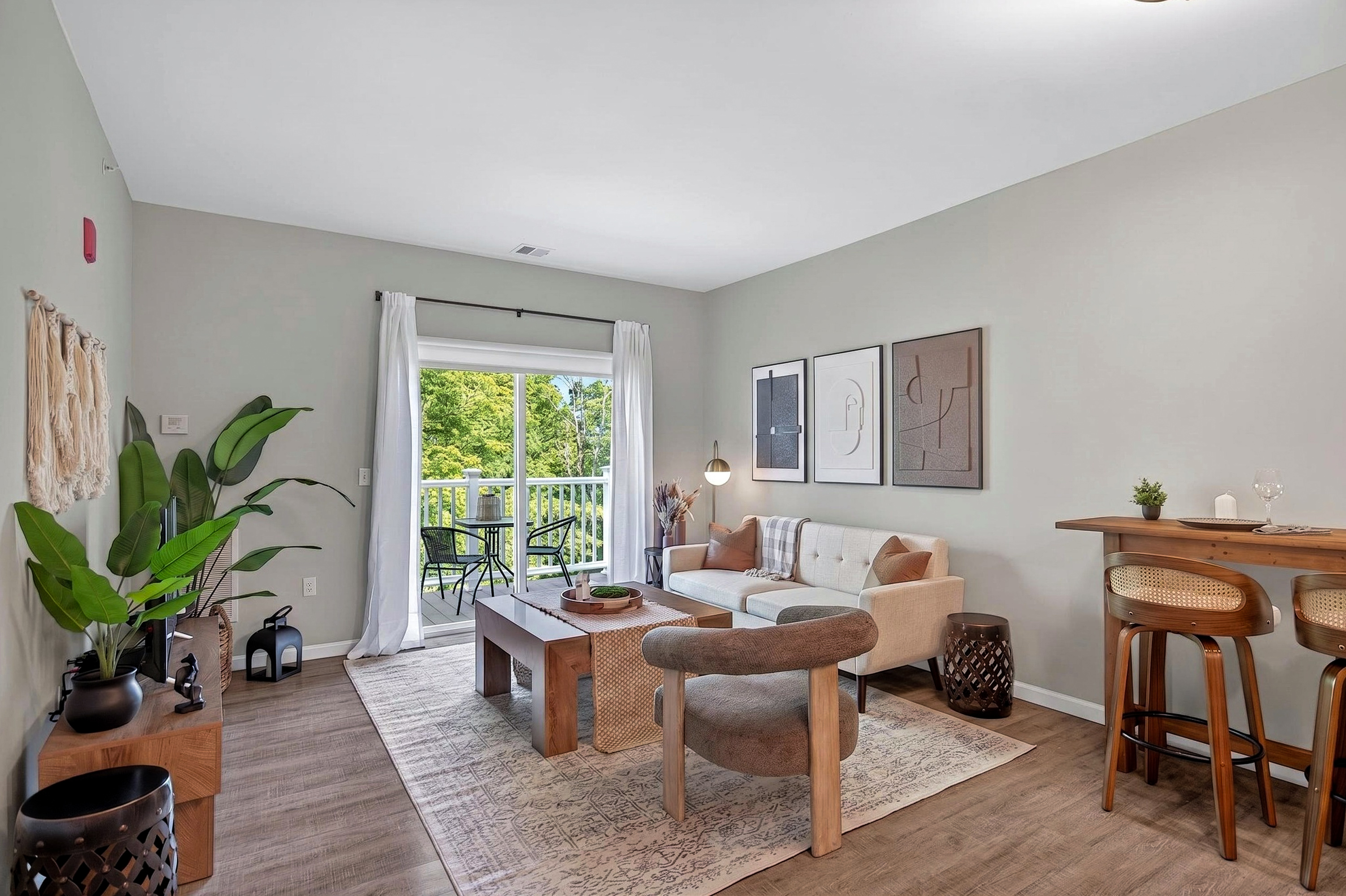 Living room with beige couch, wooden coffee table, armchair, bar stools, and sliding glass door to balcony.