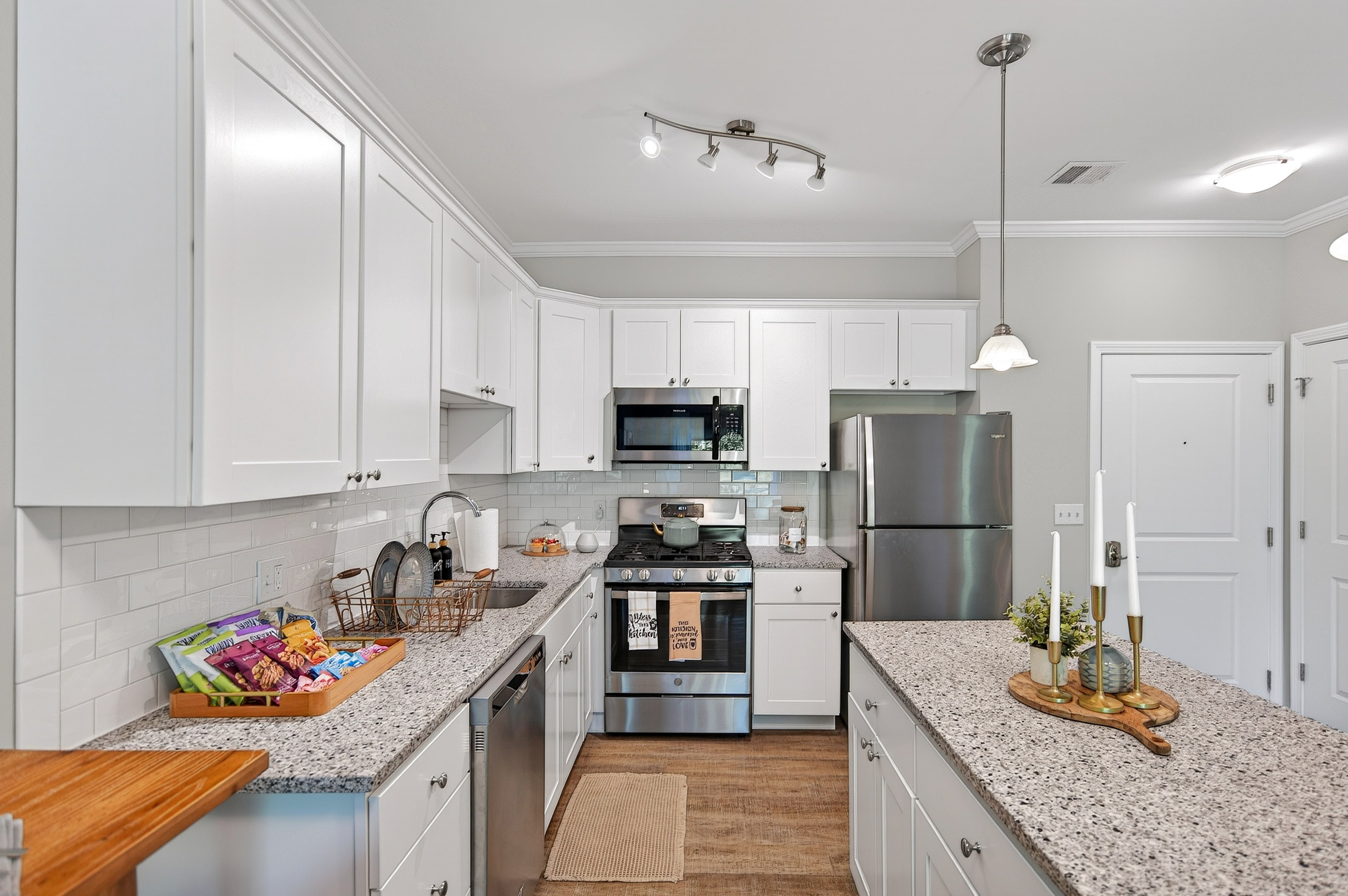 Modern kitchen with white cabinets, granite countertops, stainless steel appliances, and wooden floor.
