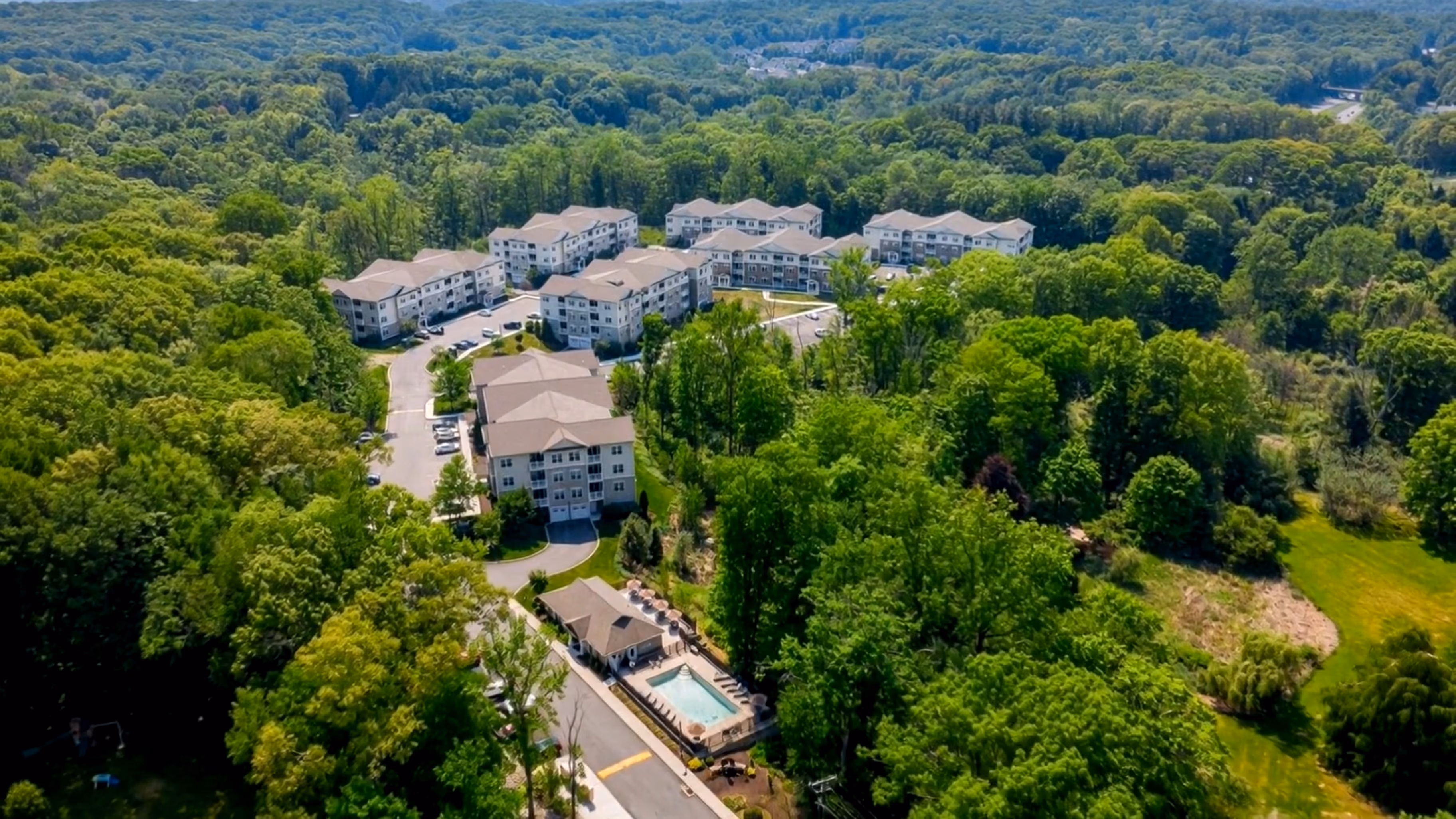 Aerial view of apartment complex surrounded by dense green trees and a swimming pool.