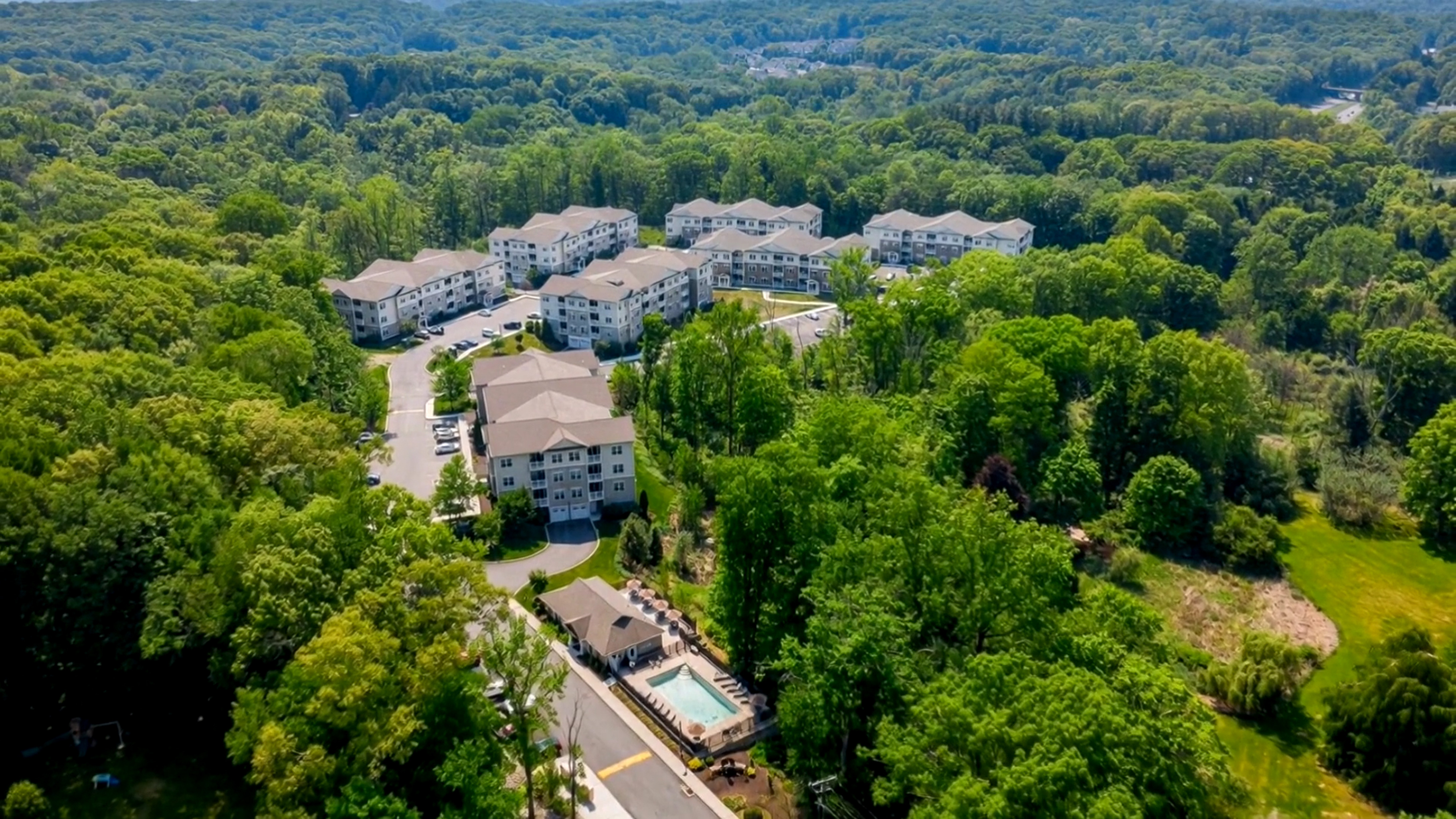 Aerial view of apartment complex surrounded by dense green trees and a swimming pool.