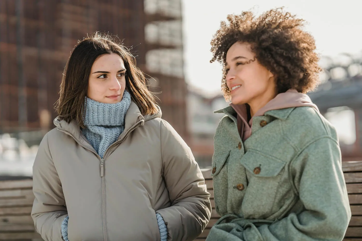 Two women wearing warm jackets walking and talking outdoors.