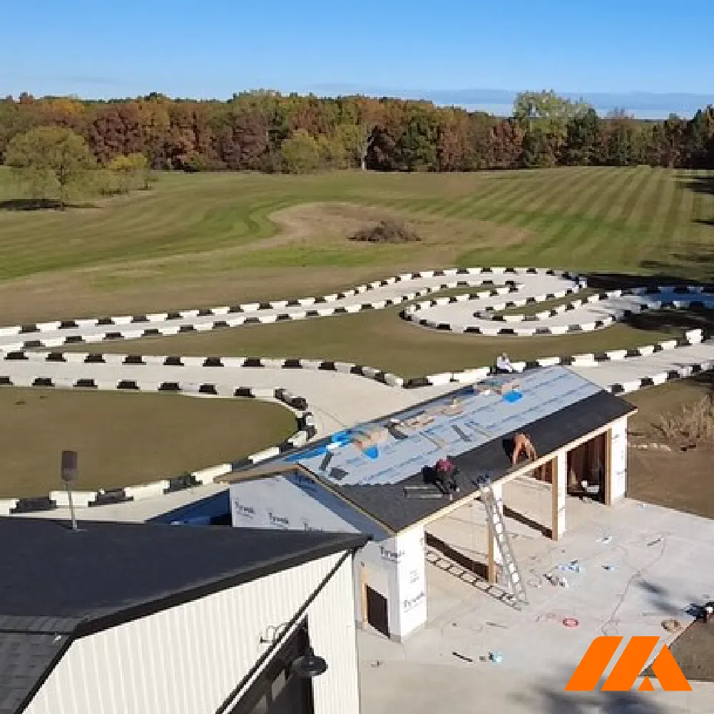 Outdoor go-kart track with white and black barriers beside a building under roof construction on a clear day.
