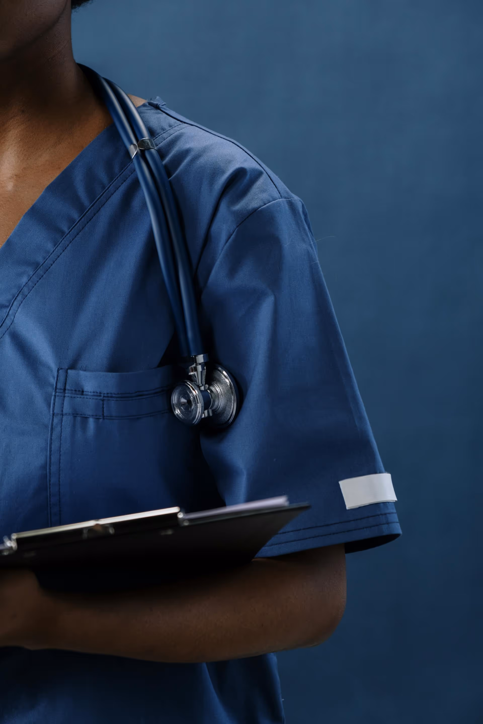 Close-up of a healthcare professional wearing blue scrubs with a stethoscope over the shoulder.