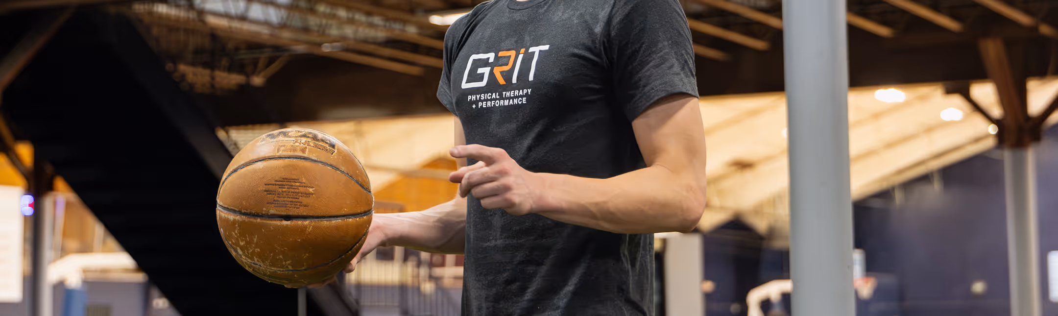Man wearing a black GRIT Physical Therapy + Performance t-shirt holding a basketball in a Richmond, VA physical therapy clinic.