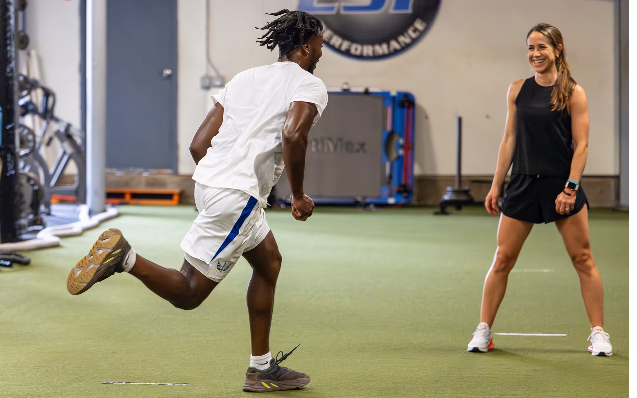 Man in white athletic wear running towards a smiling woman in black sportswear in a Richmond, VA physical therapy clinic.