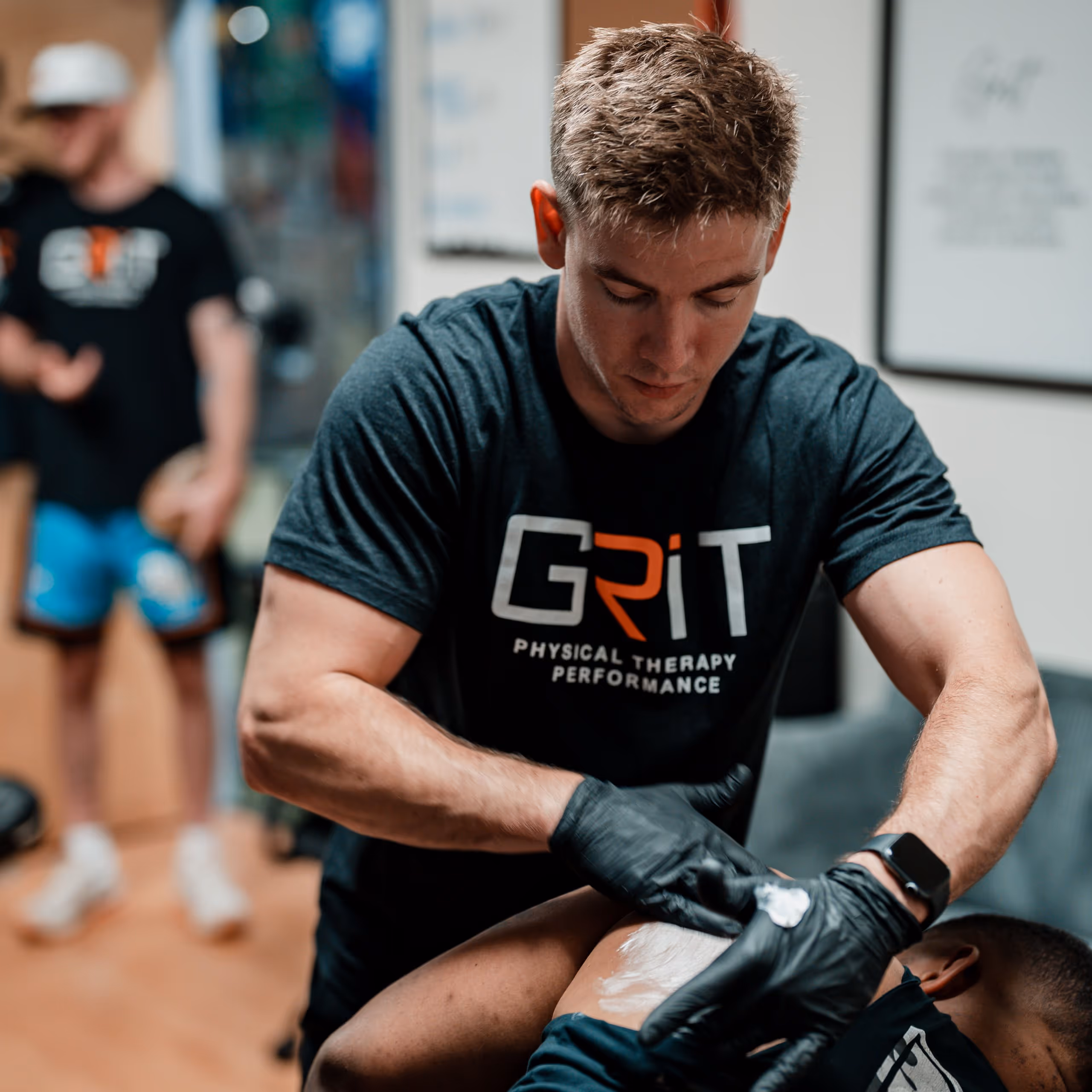 Physical therapist wearing black gloves applies cream on another person's shoulder in a Richmond, VA physical therapy clinic.
