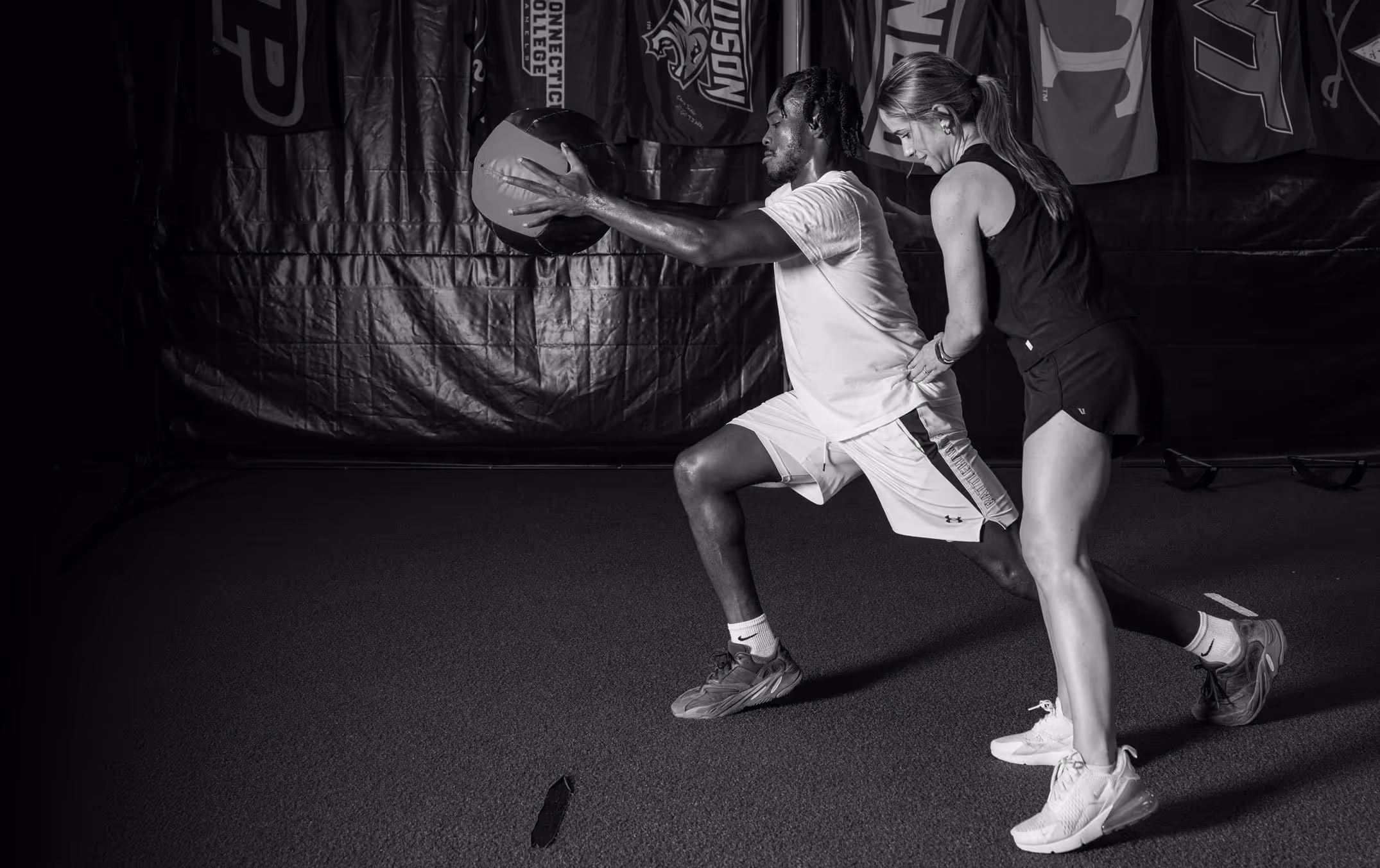 A physical therapist assists an athlete holding a medicine ball while performing a lunge exercise in a Richmond, VA physical therapy clinic.