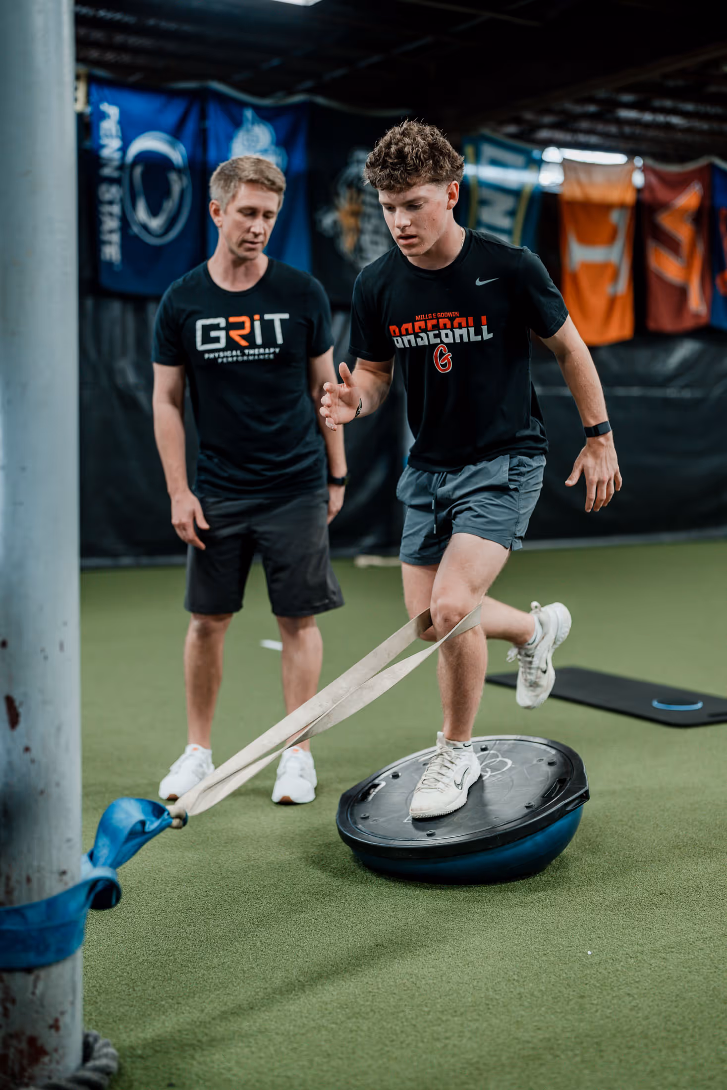 Young man balancing on a Bosu ball with a resistance band around his knee, guided by a physical therapist in a richmond physical therapy clinic
