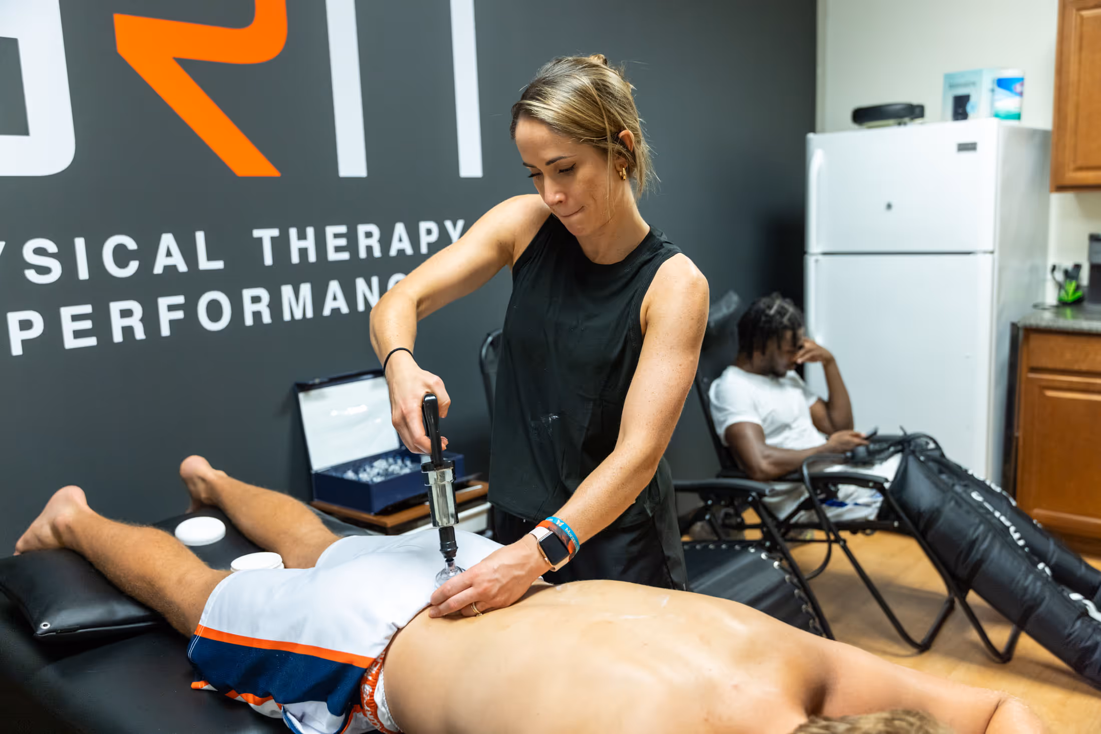 Physical therapist using a cupping device on a male patient lying face down on a massage table.