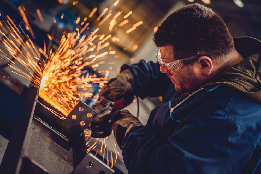 Factory worker using an angle grinder, throwing sparks — friction on the front line as a signal