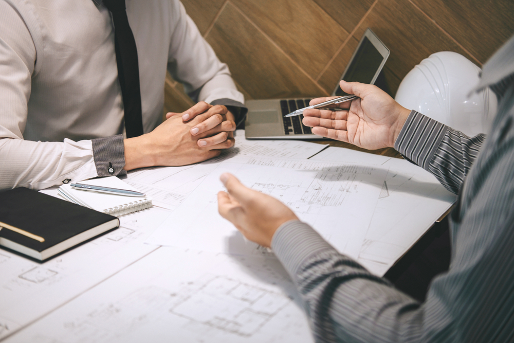 Two business partners reviewing plans and a contract across a table