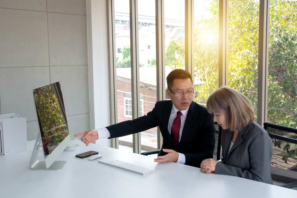 Two colleagues reviewing information on a monitor together in an office, one explaining a change to the other