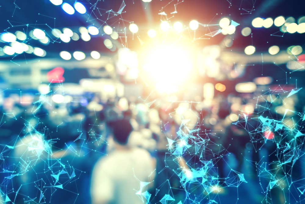 A busy trade show floor overlaid with a network graphic representing market demand