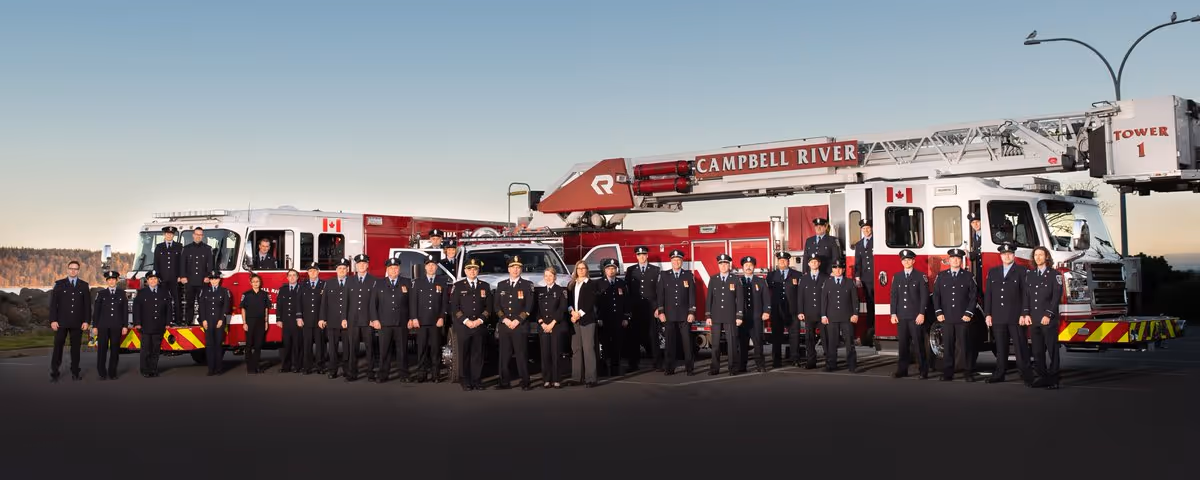 Campbell River firefighters in formal uniforms standing in front of fire apparatus for a department group photo