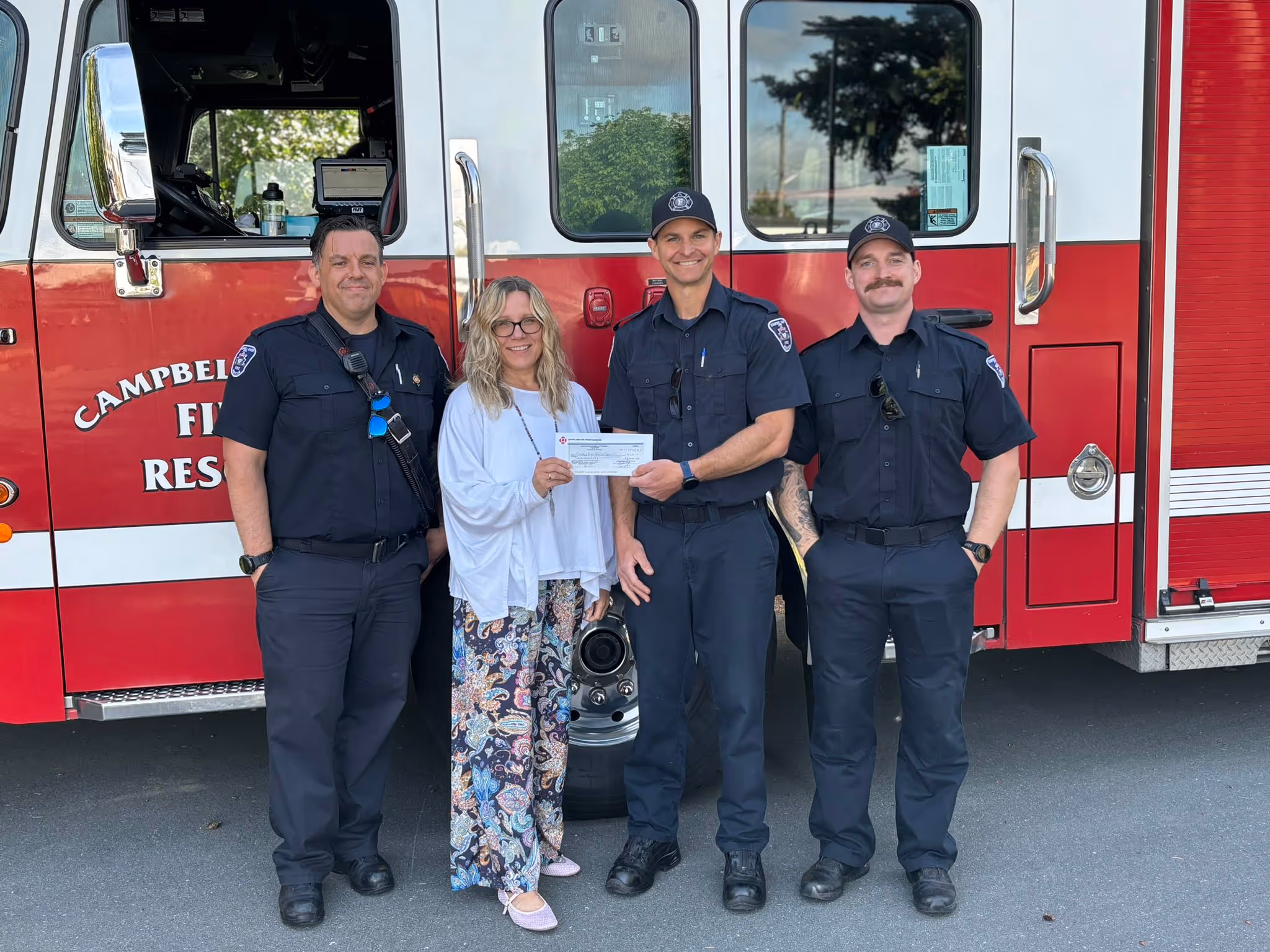 CRFFU firefighters presenting a donation check to a community member in front of a fire engine