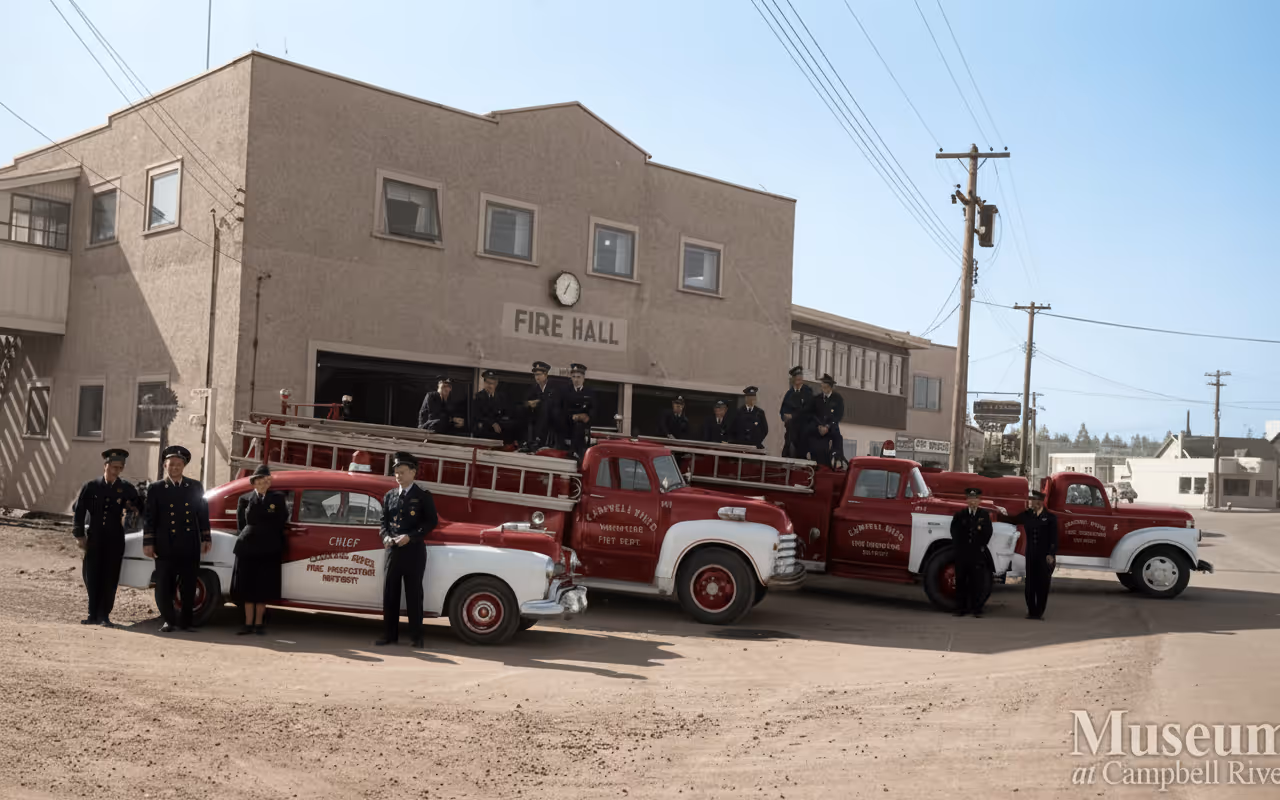 Old Campbell River Fire Hall with firefighters standing beside vintage fire trucks during a historic department photo.