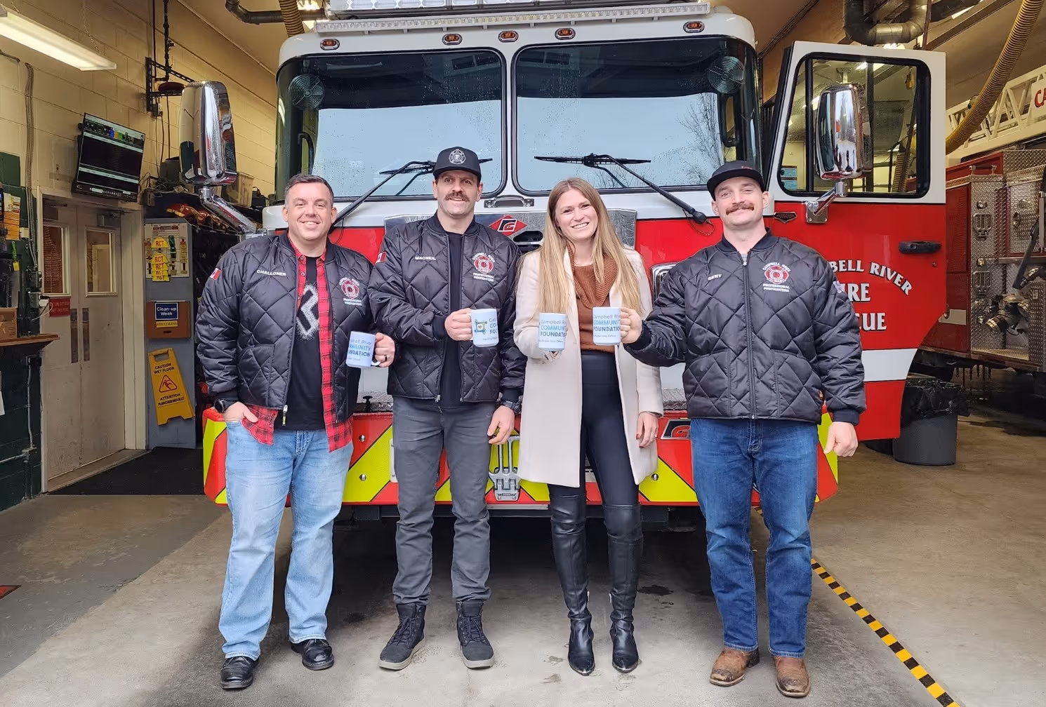 Firefighters and a community representative standing in front of a Campbell River fire engine holding donation mugs.