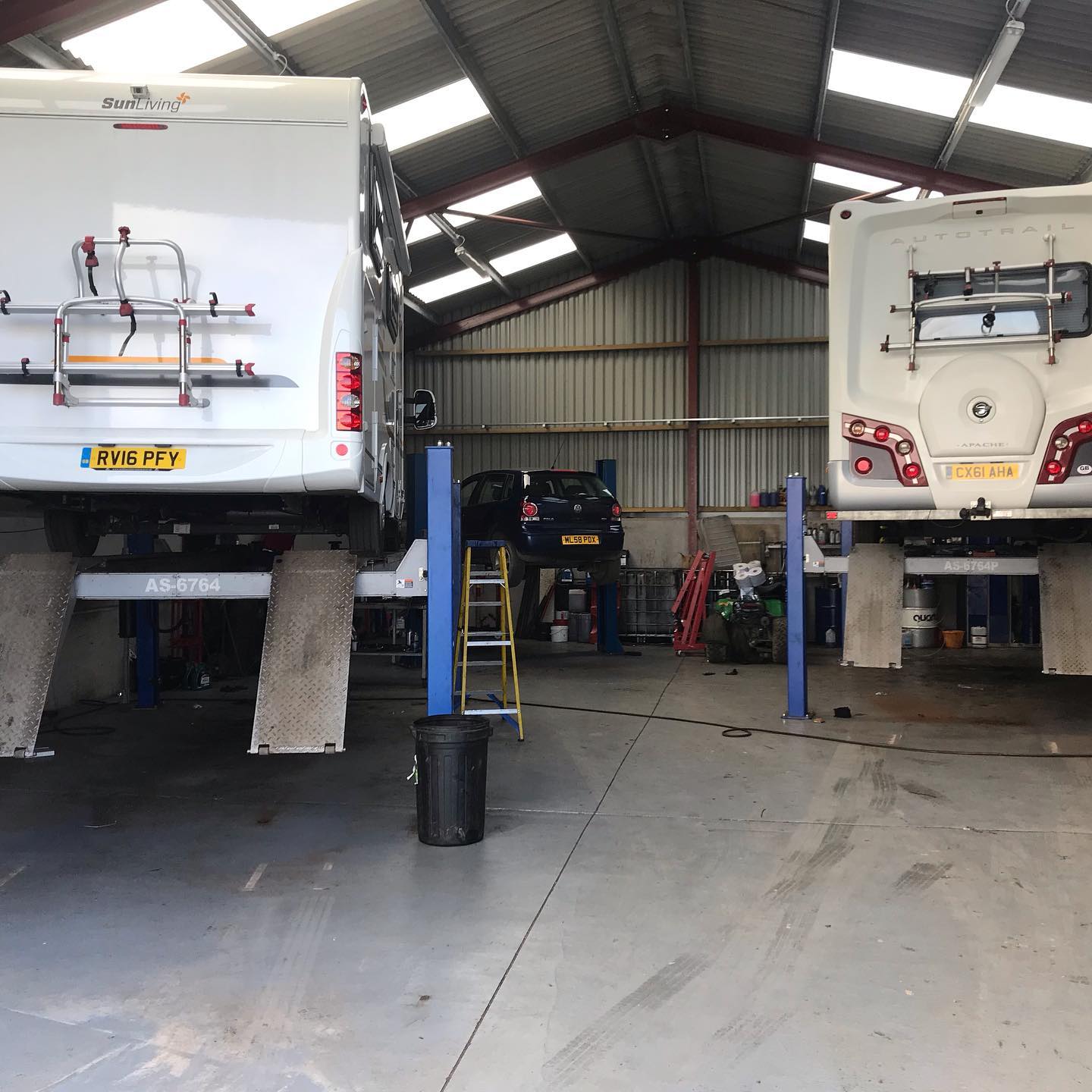 Two motorhome lifted on ramps inside a motorhome workshop