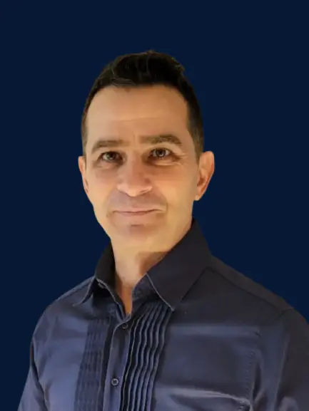 Portrait of a man with short dark hair wearing a dark blue shirt, against a solid navy background.
